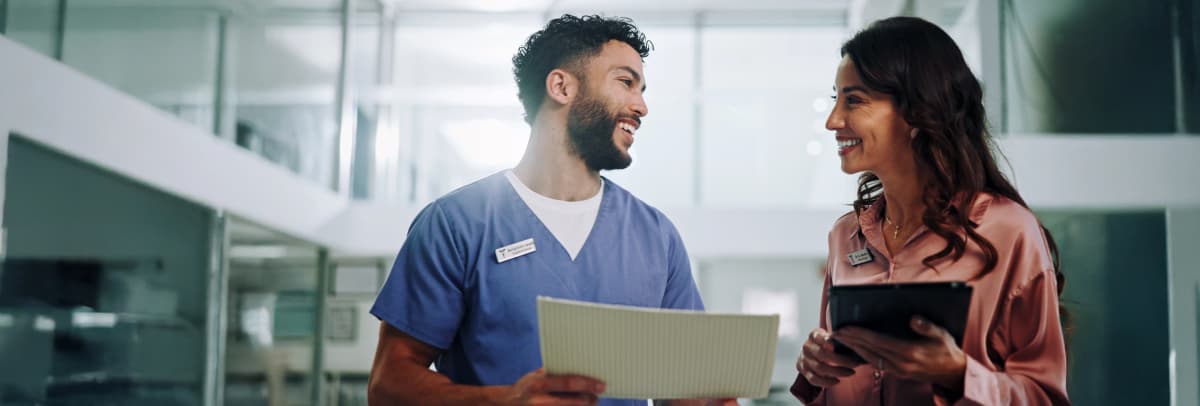 Healthcare professional and business colleague discussing patient care with digital tablet in modern hospital corridor