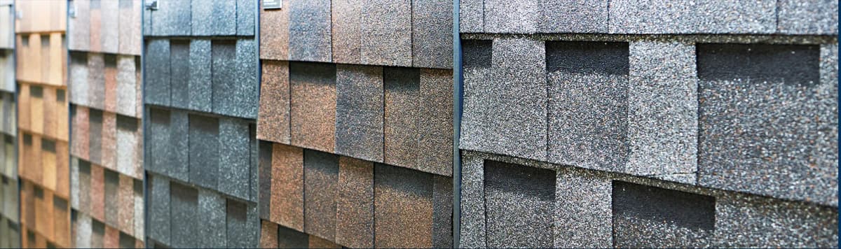Display wall showing variety of roofing shingle samples in different colors including brown tan gray and black textures