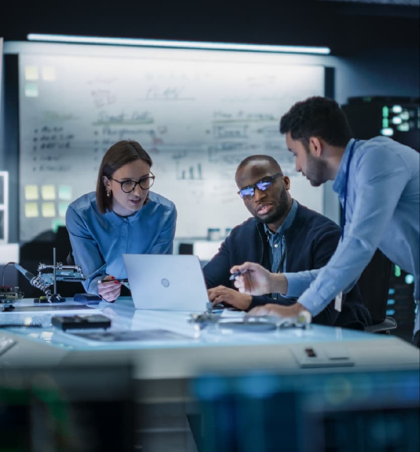 Diverse technology team collaborating on laptop with circuit boards in modern command center control room workspace